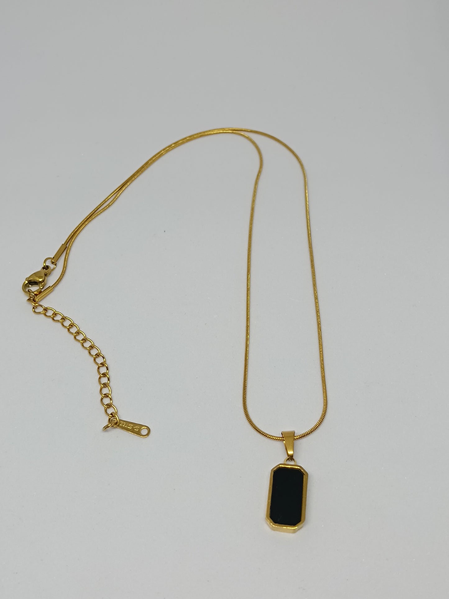 Gold necklace with a black pendant on a light gray background