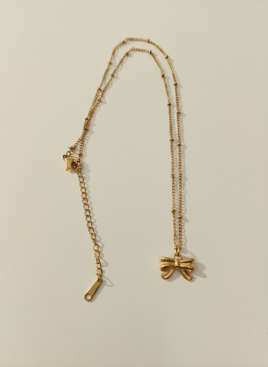 Gold necklace with a bow pendant on a light gray background