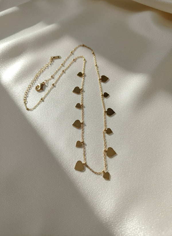 Gold necklace with heart-shaped pendants on a light gray background