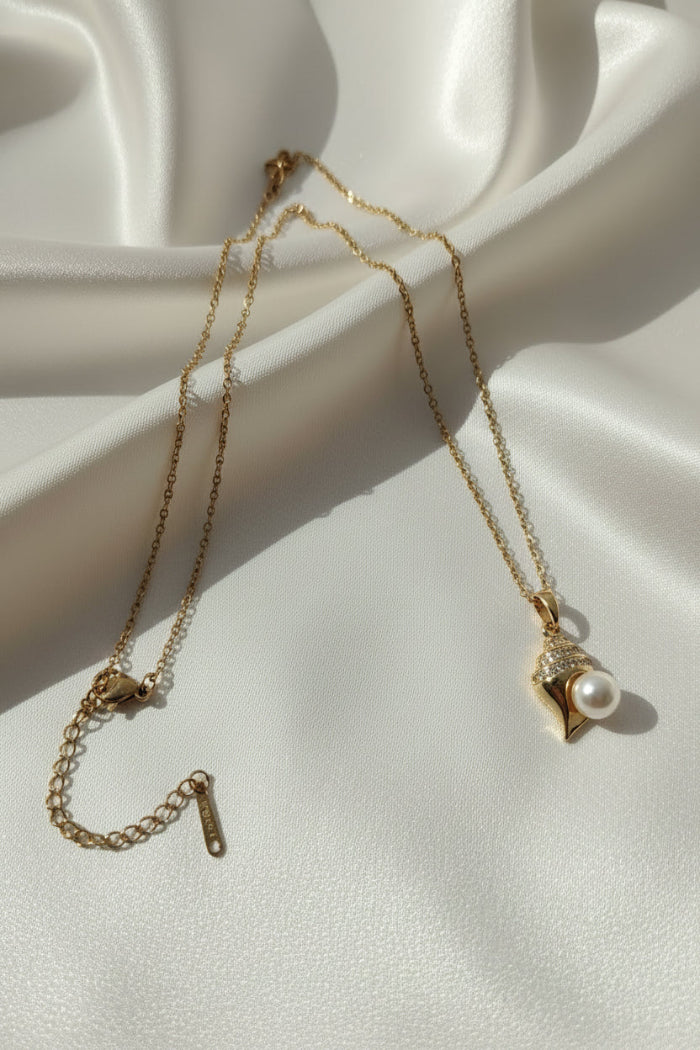 Gold necklace with a pearl pendant on a white fabric background