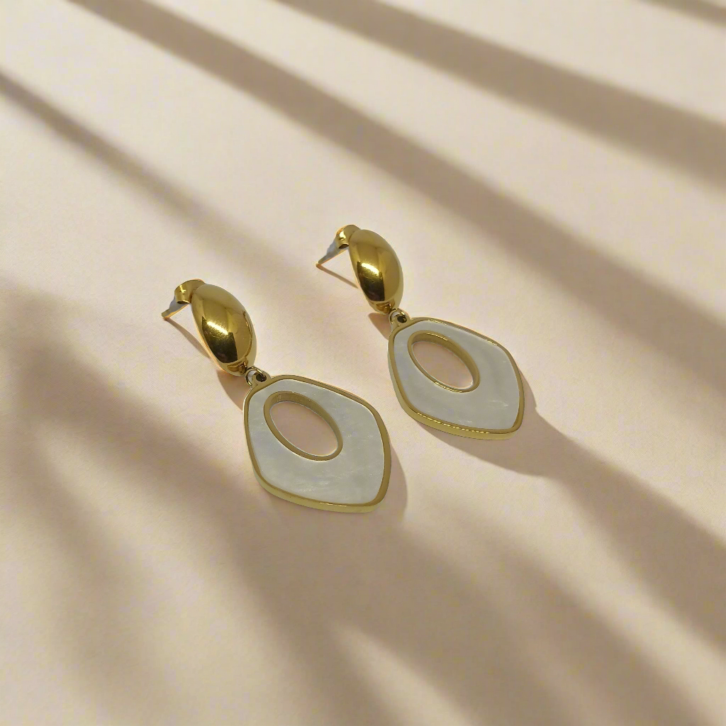 Gold and white earrings on a light gray background