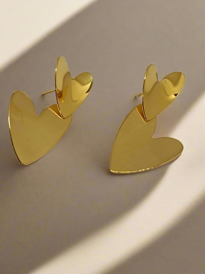 Gold heart-shaped earrings on a light gray background