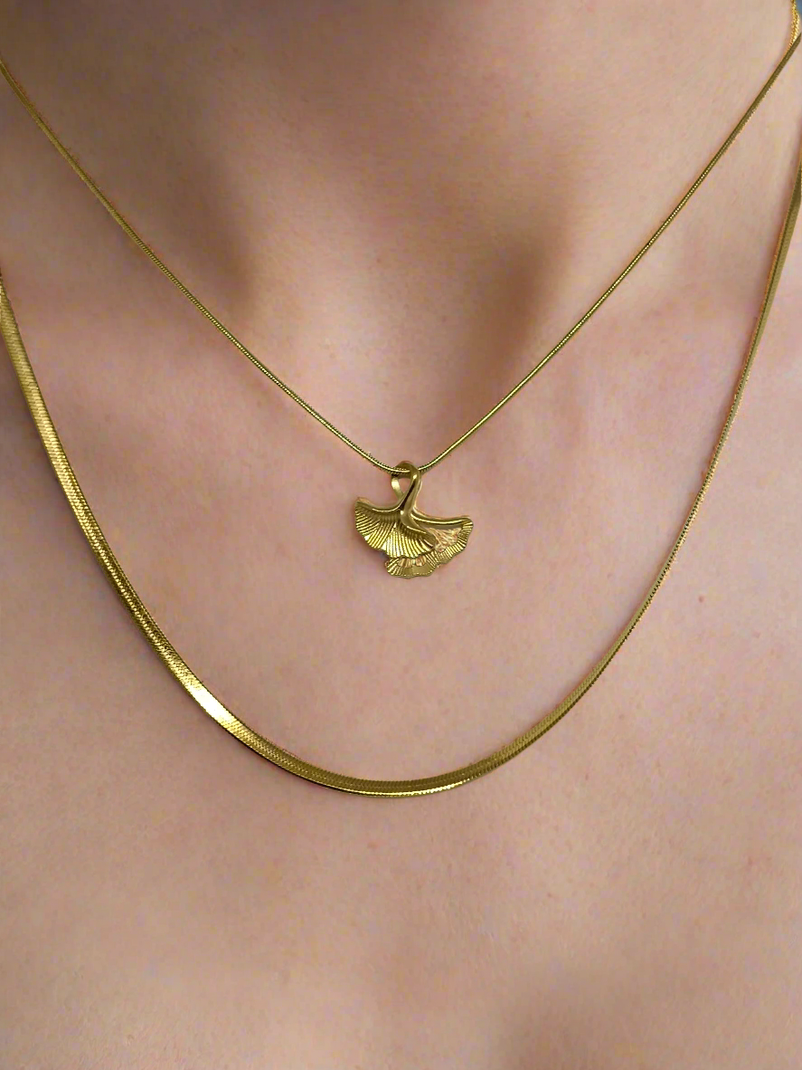 Gold necklace with a leaf pendant on a person's neck