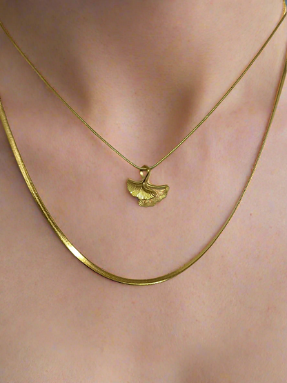 Gold necklace with a leaf pendant on a person's neck