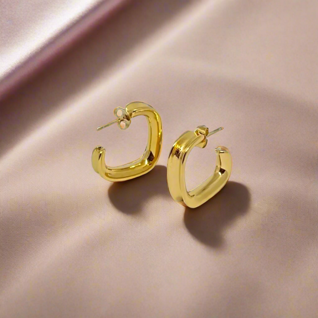 Gold hoop earrings on a soft pink and orange gradient background