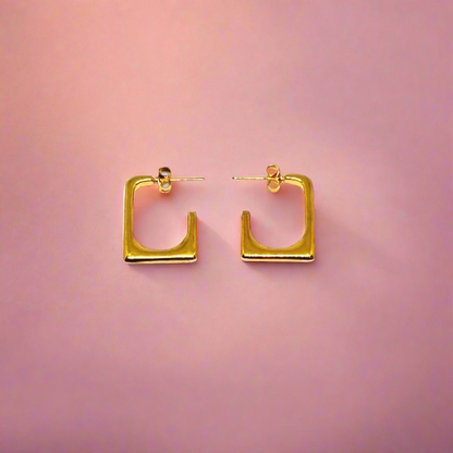 Gold hoop earrings on a soft pink and orange gradient background