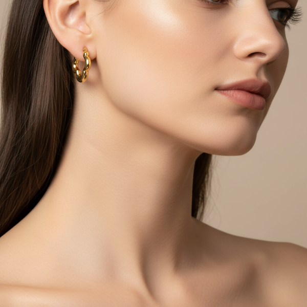 Close-up of a woman wearing golden hoop earrings against a neutral background