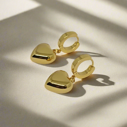 Gold heart-shaped earrings on a light gray background