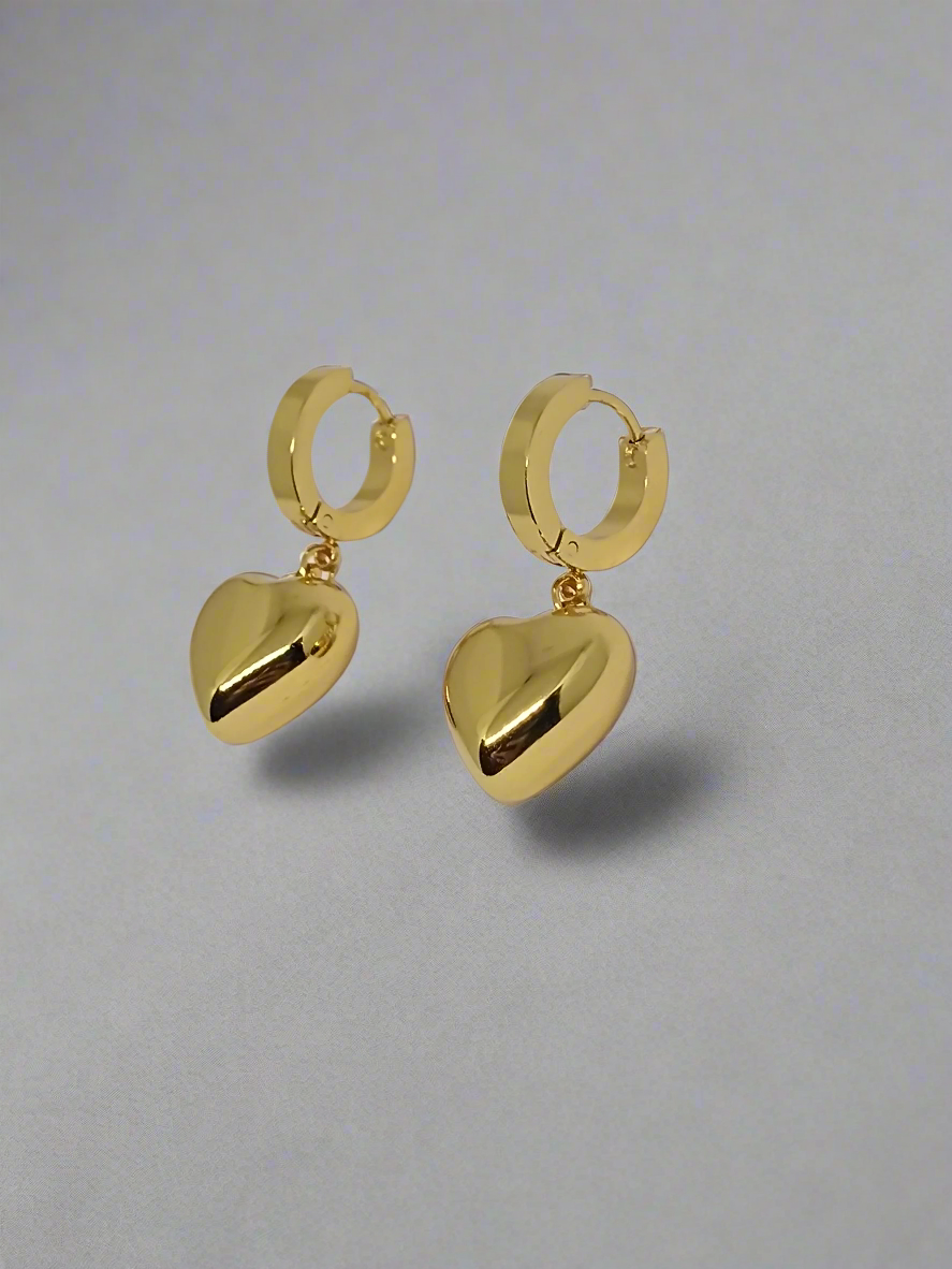 Gold hoop earrings with heart-shaped drops on a light gray background