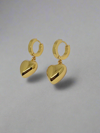 Gold hoop earrings with heart-shaped drops on a light gray background