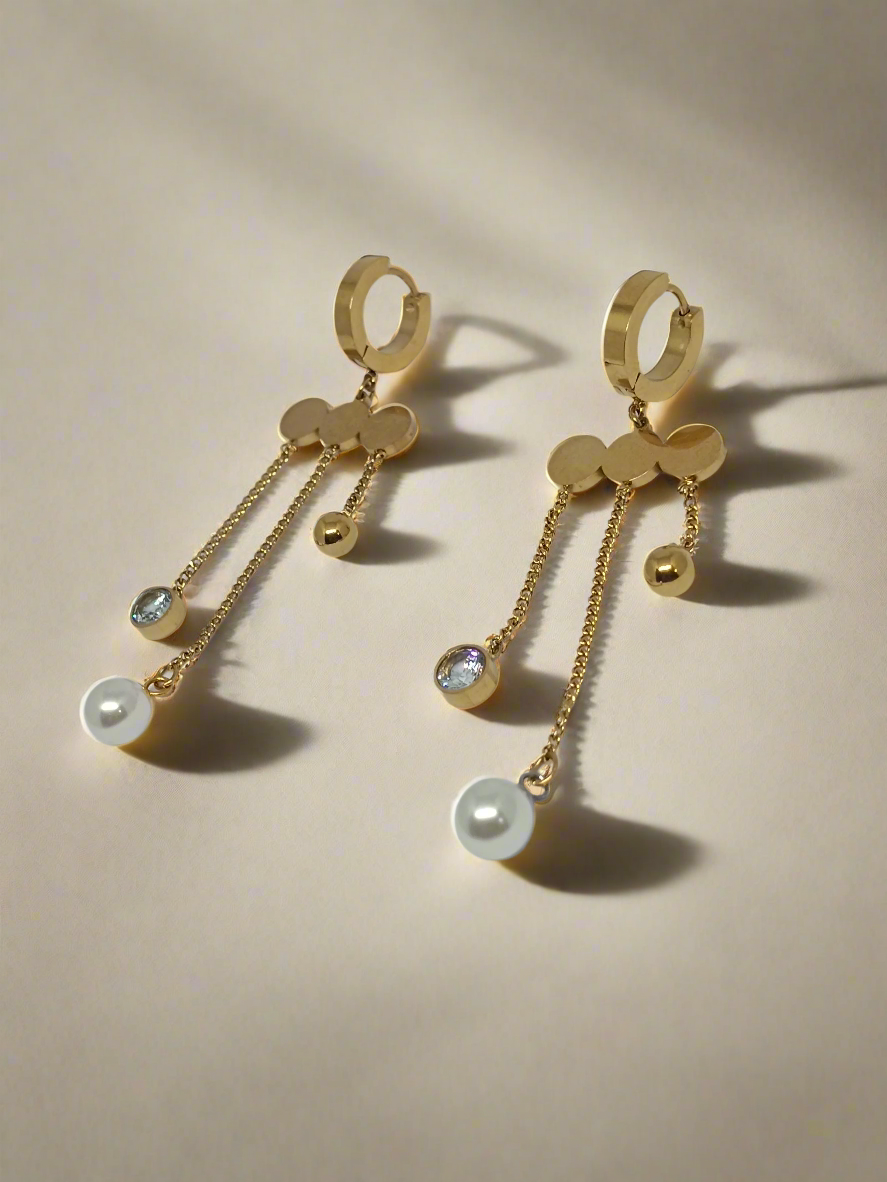 Gold earrings with pearl drops on a light gray background