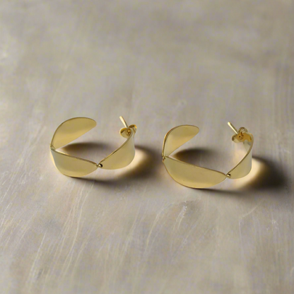Golden half hoop earrings on a beige background