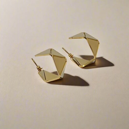 Gold geometric hoop earrings on a light gray background