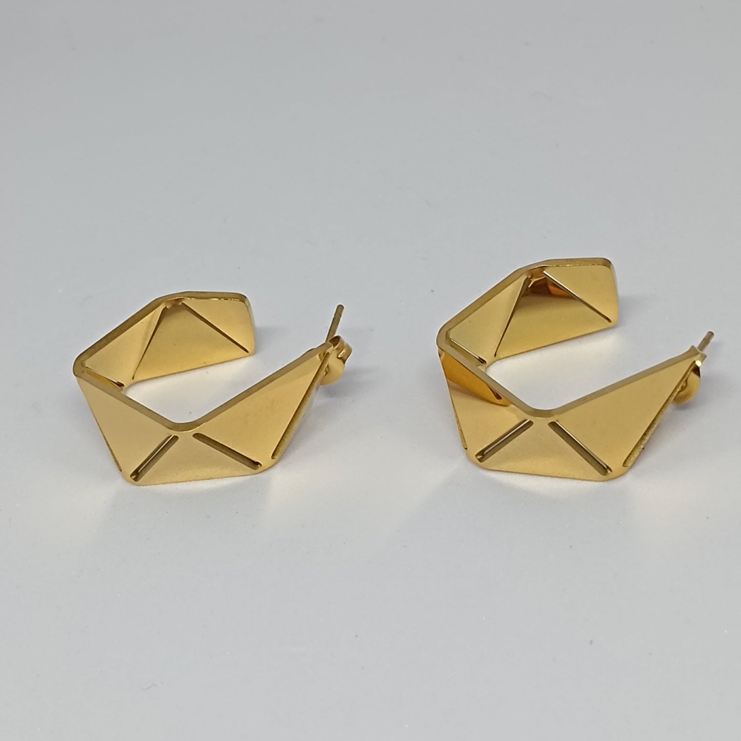 Gold geometric hoop earrings on a light gray background