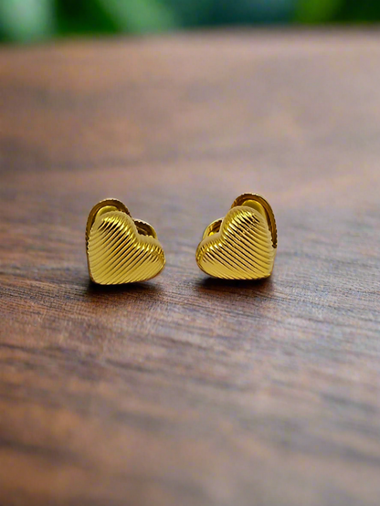 Gold heart-shaped earrings on a pink background