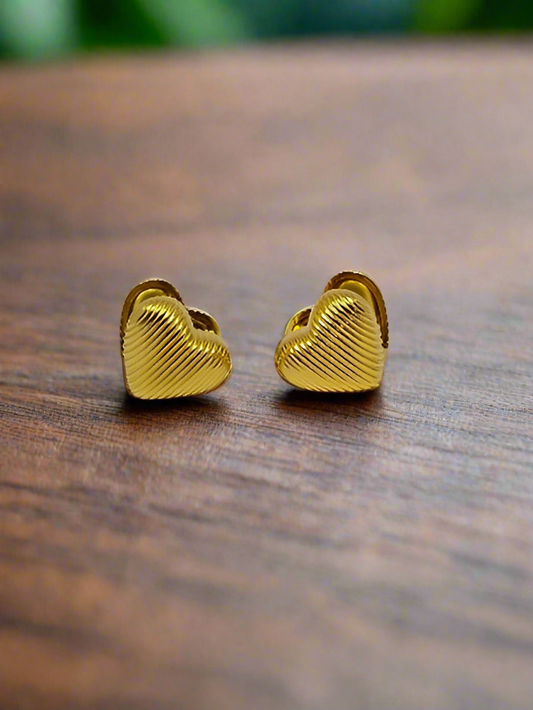 Gold heart-shaped earrings on a pink background