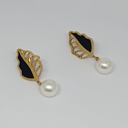 Gold leaf-shaped earrings with black centers and pearl drops on a light gray background