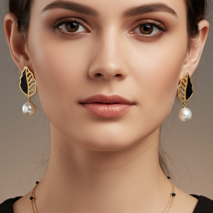 Close-up of a woman wearing golden earrings with black and pearl details on a neutral background