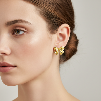 Golden bow-shaped earrings worn by a model on a neutral background