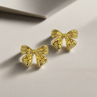Gold bow-shaped earrings on a light gray background