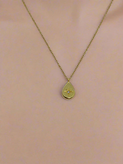 Gold necklace with a teardrop-shaped pendant on a white background