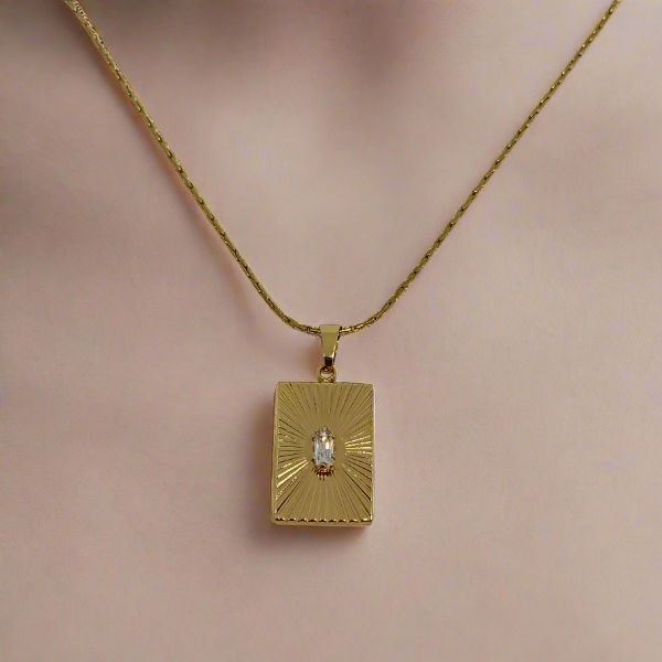 Gold necklace with a rectangular pendant on a light gray background