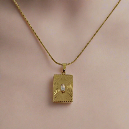 Gold necklace with a rectangular pendant on a light gray background