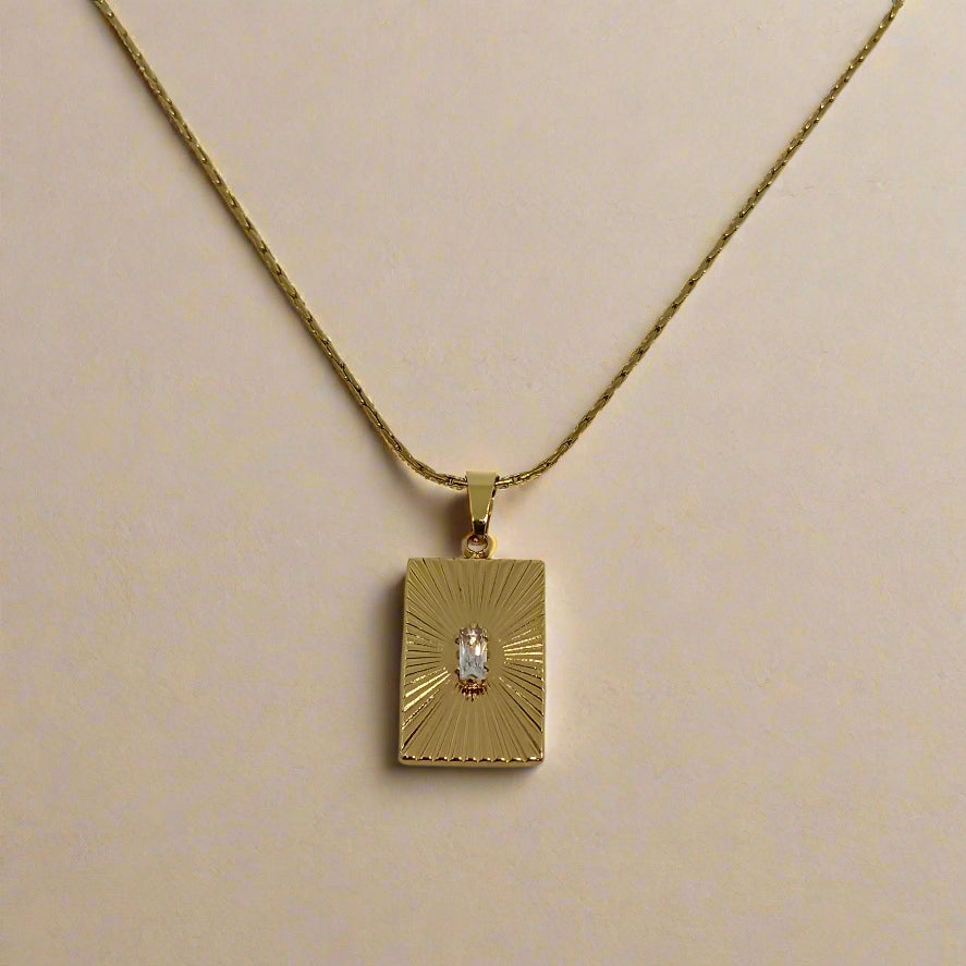 Gold necklace with a rectangular pendant on a light gray background