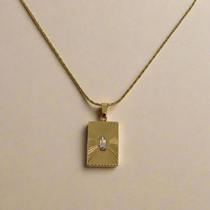 Gold necklace with a rectangular pendant on a light gray background