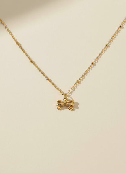 Gold bow necklace on a beige background