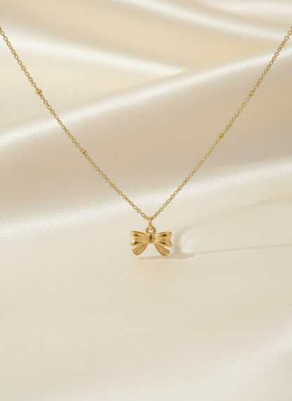Gold bow-shaped pendant necklace on a beige fabric background