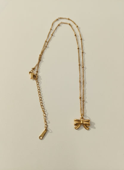 Gold necklace with a bow pendant on a light gray background