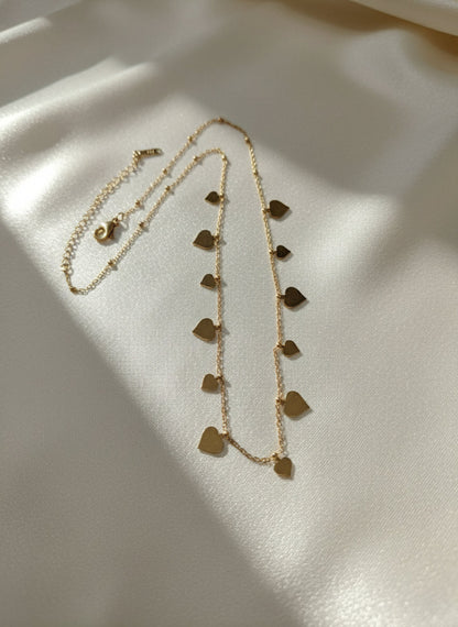 Gold necklace with heart-shaped pendants on a light gray background
