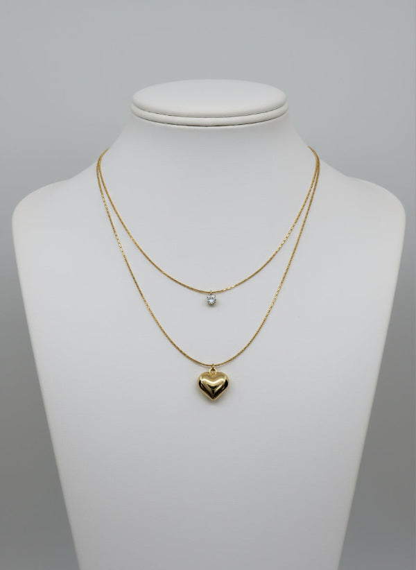 Golden necklaces with heart pendants on a mannequin bust against a gray background