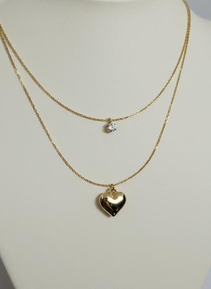 Layered golden necklaces with heart and round pendants on a mannequin.