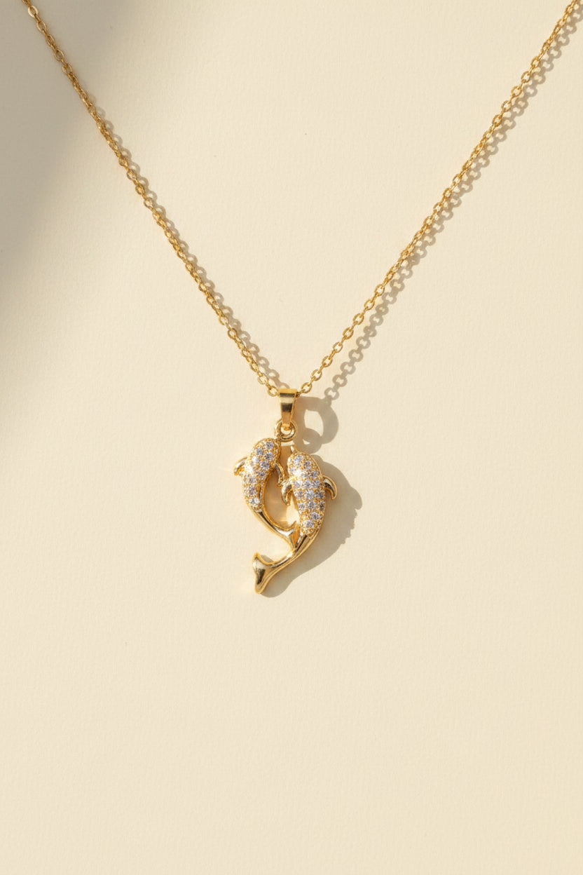 Gold necklace with a dolphin pendant on a beige card
