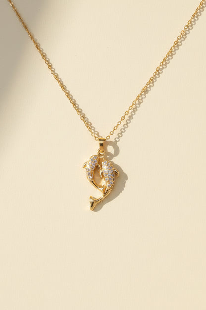 Gold necklace with a dolphin pendant on a beige card