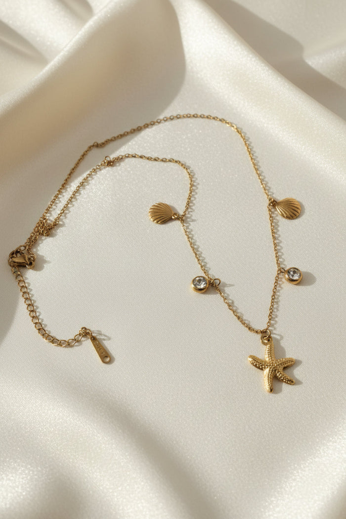 Golden necklace with starfish and shell charms on a white background