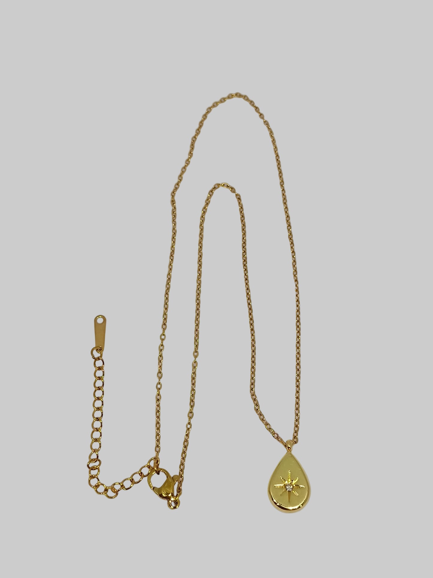 Gold necklace with a teardrop pendant on a light gray background