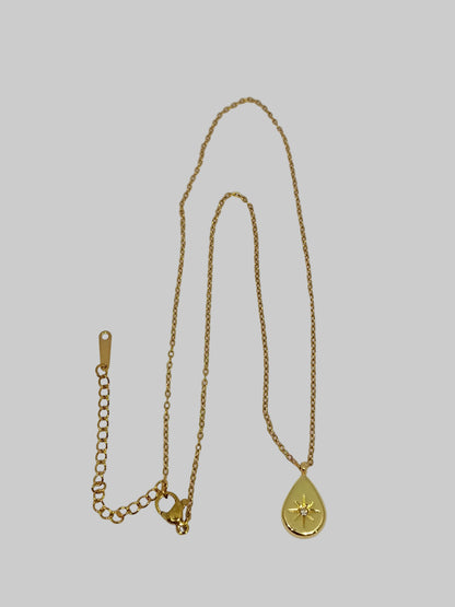 Gold necklace with a teardrop pendant on a light gray background